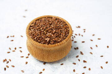 Brown flaxseeds in a wooden bowl on a light surface with scattered seeds