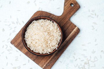 Rice in a wooden bowl on a cutting board with scattered grains