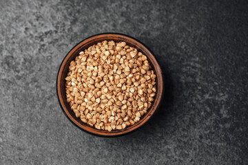 Buckwheat grains in a wooden bowl on a dark surface for culinary use