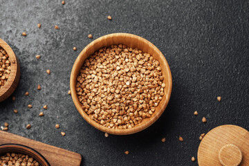 Buckwheat grains in wooden bowl on dark stone background