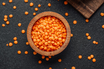 Orange lentils in a wooden bowl on a dark surface with scattered grains