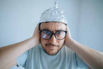 Man wearing aluminum foil hat demonstrates conspiracy theory paranoia with humorous expression in...