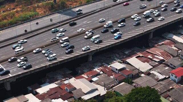 Drone view of heavy traffic speeding above crowded slum housing. Strong contrast between wealth and poverty in a fast-growing metropolis.