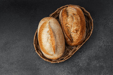 Freshly baked artisan bread rolls in a woven basket on a dark surface