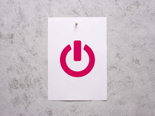 White sheet of paper with start power symbol pinned to a white concrete wall.