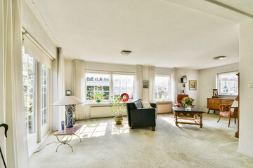 A spacious living room featuring natural light streaming through large windows, elegant furniture, and decorative plants creating a warm atmosphere.
