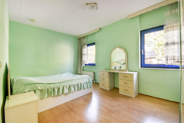 A serene and minimalist green bedroom featuring a bed with a soft cover, a matching dresser, and large windows that allow natural light to fill the space.