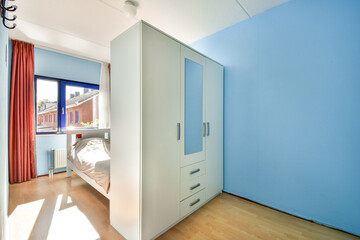 A modern bedroom featuring light blue walls, white furniture, and large windows, creating a bright and airy atmosphere. The design emphasizes simplicity and functionality.