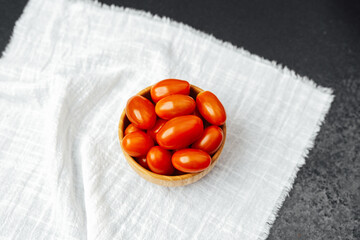Fresh cherry tomatoes in a wooden bowl on a light fabric texture