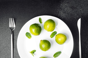 Fresh limes arranged on a white plate with mint leaves on a dark table