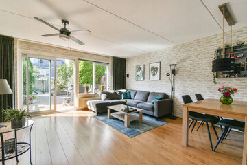 Stylish living room featuring a cozy sofa, a wooden dining table, and large windows providing a lush garden view, creating an inviting atmosphere.