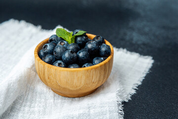 Fresh blueberries in a wooden bowl with mint leaf on a fabric napkin