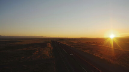 A striking aerial view of a highway stretching through a vast desert landscape under a golden sunset. The warm hues and long shadows create a dramatic and serene atmosphere.