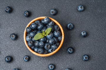 Fresh blueberries in wooden bowl with mint on dark surface