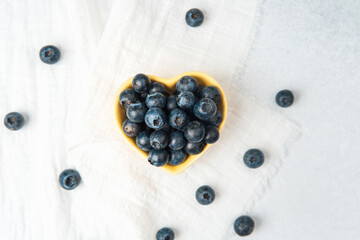 Fresh blueberries arranged in a heart-shaped bowl on a light backdrop