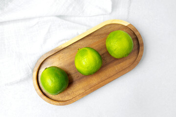 Fresh limes arranged on a wooden tray against a light background