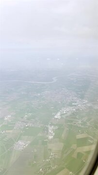 View from airplane window flying over Suzzara city and River Po, showcasing the vast green farmland, winding river, and cloudy horizon during descent towards Verona airport