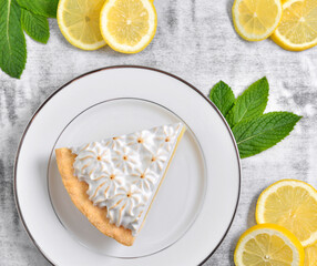 Slice of lemon meringue pie with sliced lemons and mint