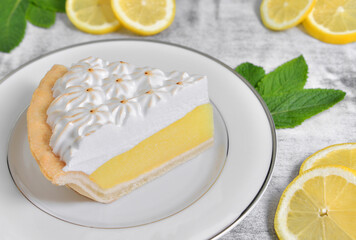 Slice of lemon meringue pie with sliced lemons and mint