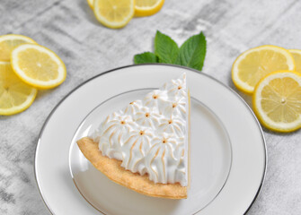 Slice of lemon meringue pie with sliced lemons and mint