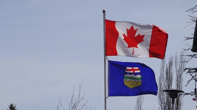 The Canadian flag and the flag of Alberta are displayed on flagpoles against a clear sky, representing national and provincial identity.