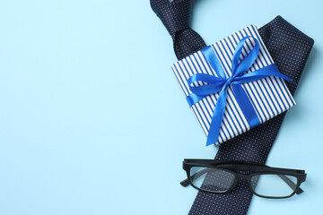 Top view photo of giftbox with silk ribbon bow, glasses and elegant tie on color background