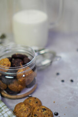 an open jar filled with cookies, and some cookies outside the jar, with flour sieve and milk bottles in the background