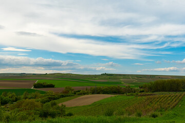 Vast rolling hills adorned with vibrant green fields under a dramatic sky near a tranquil countryside village at midday