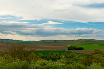 Obraz premium Expansive countryside landscape featuring rolling hills and vibrant green fields under a cloudy sky