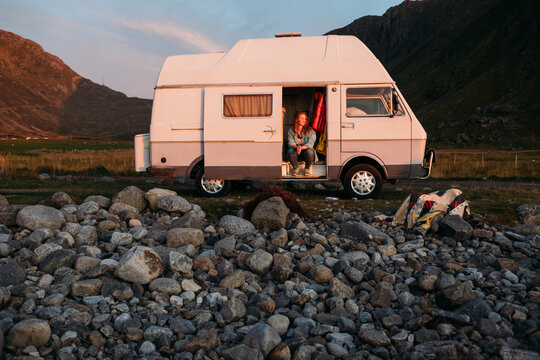 Woman sitting in van doorway surrounded by rocky terrain