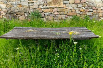 Weathered wooden table stands amidst lush green grass and wildflowers in a serene garden setting near an ancient stone wall