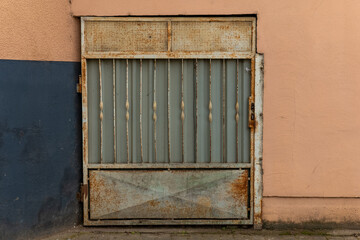 Rusty metal gate with vertical bars against a textured wall in an urban setting