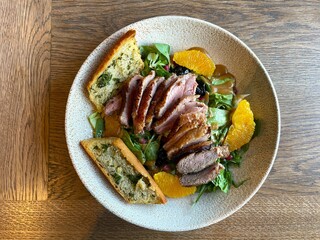 A delicious dish of grilled meat, orange, greens and croutons on the table in a restaurant