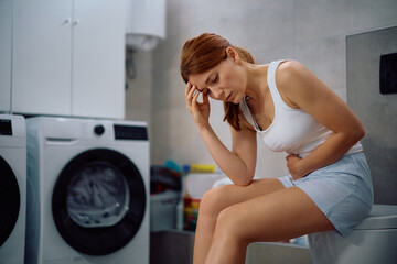 Worried woman holding her abdomen in pain in bathroom.