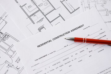 Pen on residential construction agreement and planning blueprints of residential building project