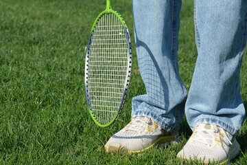 Unrecognizable person standing on the grass with kneeled jeans, holding a badminton racket. Concept...