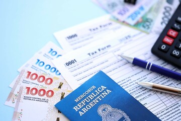 Argentine pesos money bills in big amount lies on table with pen, calculator, passport and tax forms
