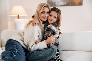 Cozy, sitting on the sofa, side view. Mother and daughter are together in domestic room