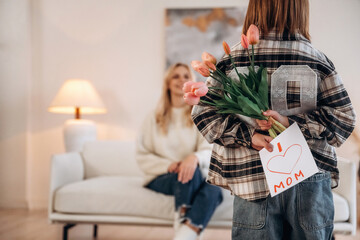 Hiding flowers and gift card for mom. Mother and daughter are together in domestic room