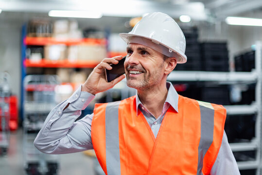 Warehouse manager in safety vest and hard hat talking on mobile phone
