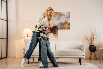 In casual clothes, standing and embracing. Mother and daughter are together in domestic room