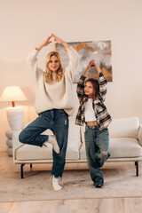 Naklejka premium Standing on one leg, sport and yoga. Mother and daughter are together in domestic room