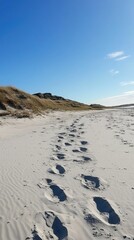 Footprints in sand, dunes, blue sky.