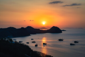 A stunning sunset brilliantly paints golden hues across the tranquil, serene waters, which are dotted with yachts, boats and silhouetted hills in the scenic background, Labuan Bajo, Komodo, Indonesia