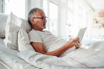 Senior man in bed using a tablet indoors during the day
