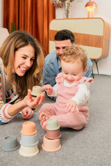 Joyful family moments as a baby explores colorful stacking cups with loving parents during playful...