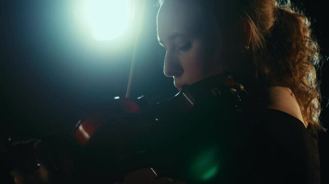 Beautiful inspired woman playing violin alone in darkness, romantic love song. Fascinating slow motion shot with talented lady performing classical melody by violin, traditional music performance