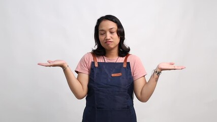 Young female barista wearing a navy apron making a confused expression, raising both hands in a shrug gesture. Studio shot with white background, representing doubt, uncertainty, or not knowing