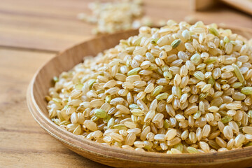 closeup dry brown short grain unpolished rice or Japanese brown rice in wood bowl on wooden table rustic background with copy space