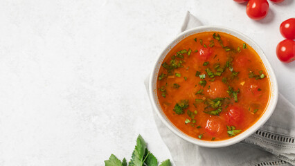 Vegetable fresh soup with tomatoes and herbs in white bowl on linen napkin. Copy space